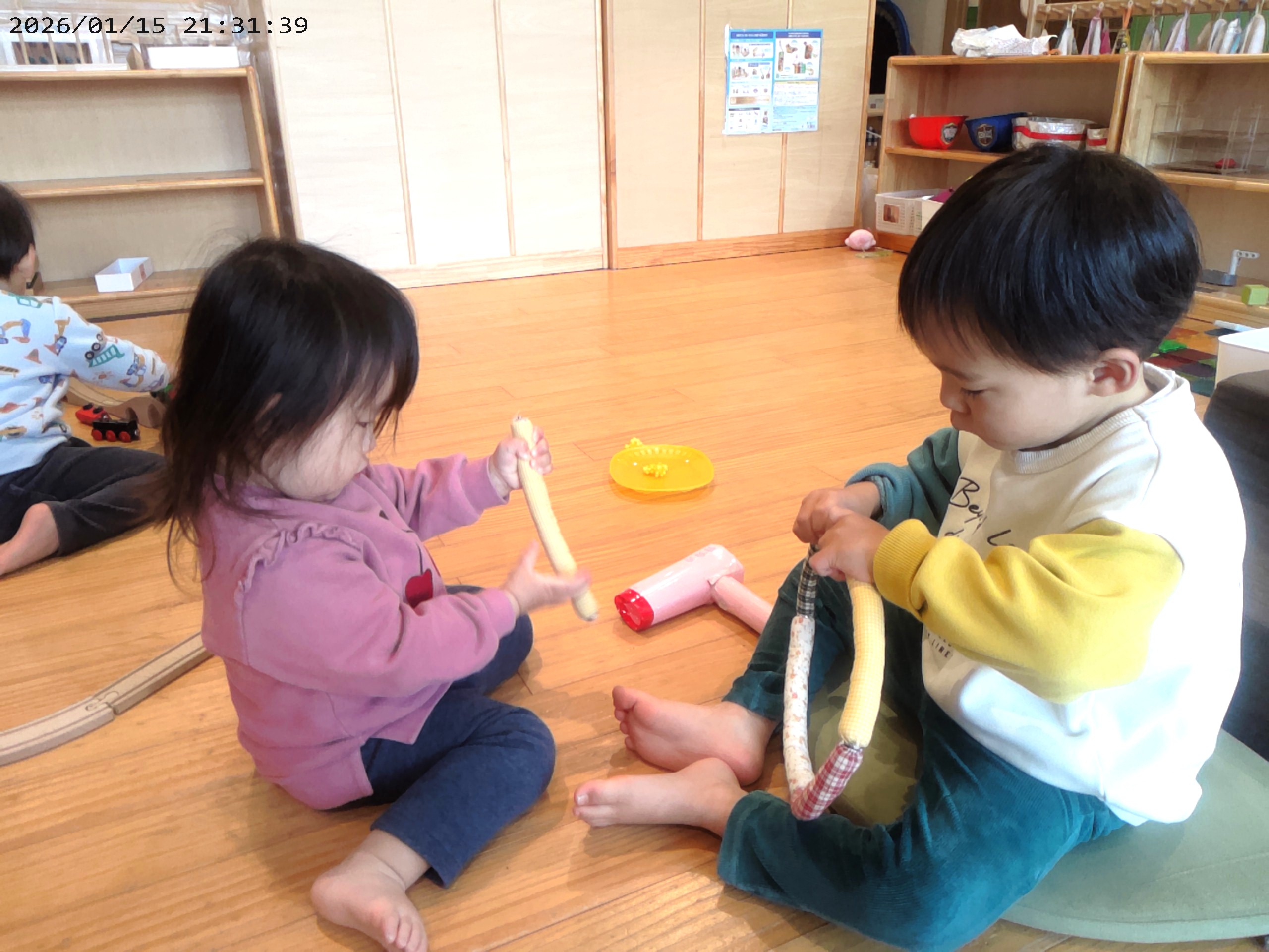 2歳児さんがボタンを留めているのを一生懸命観察する1歳児さん。真似っこする姿がかわいいです！